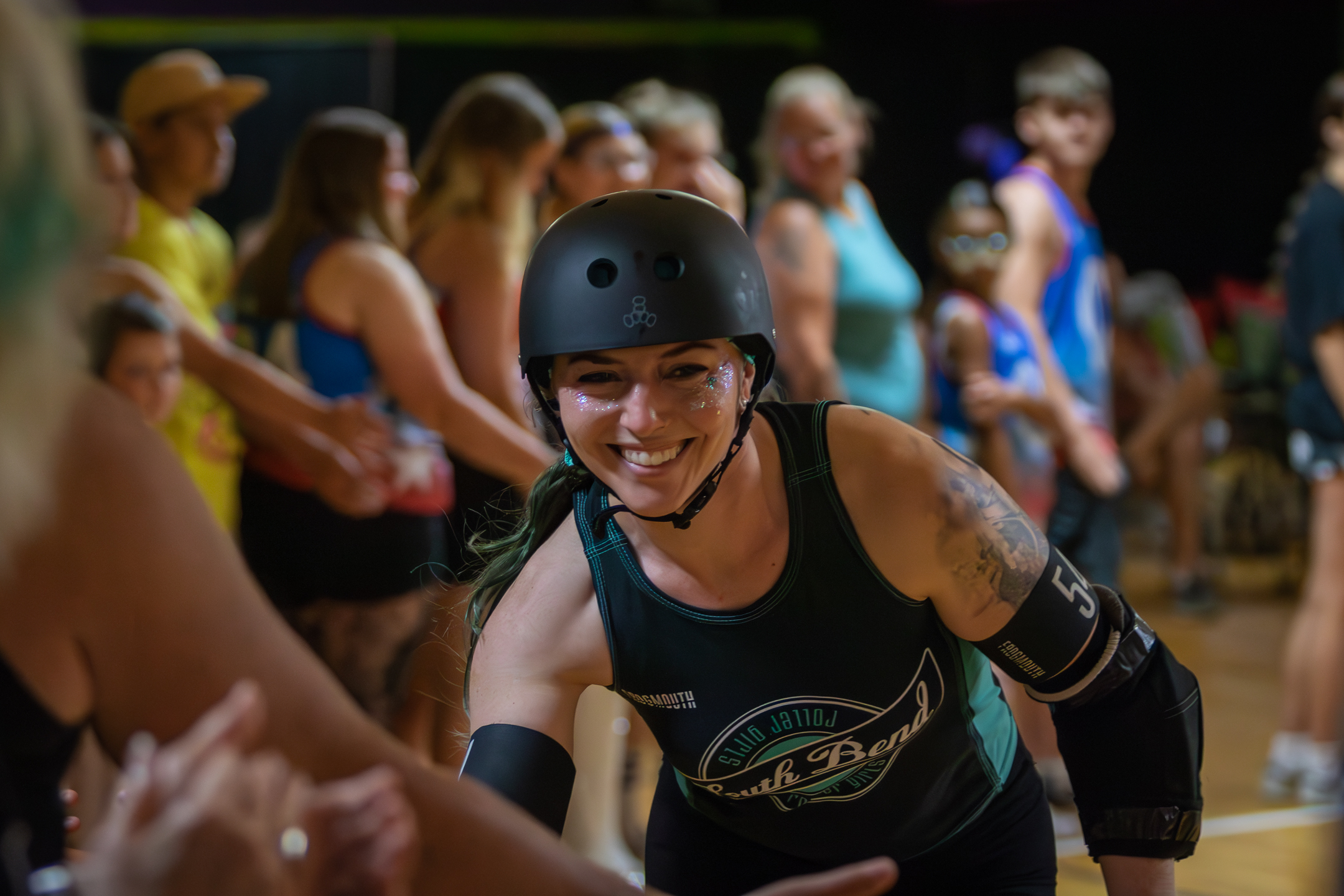 A roller derby skater in helmet and pads smiling at fans during a bout