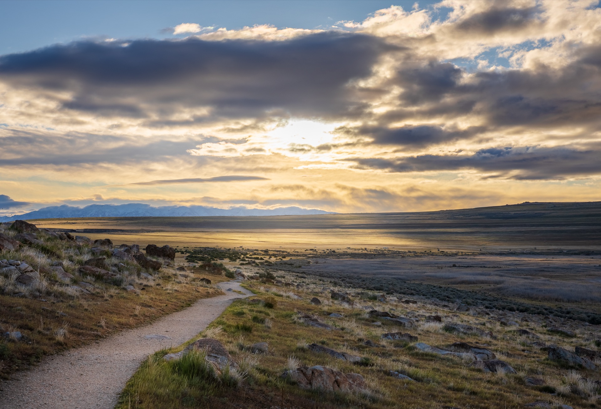 Evening light over a high plain, a footpath winding toward distant mountains