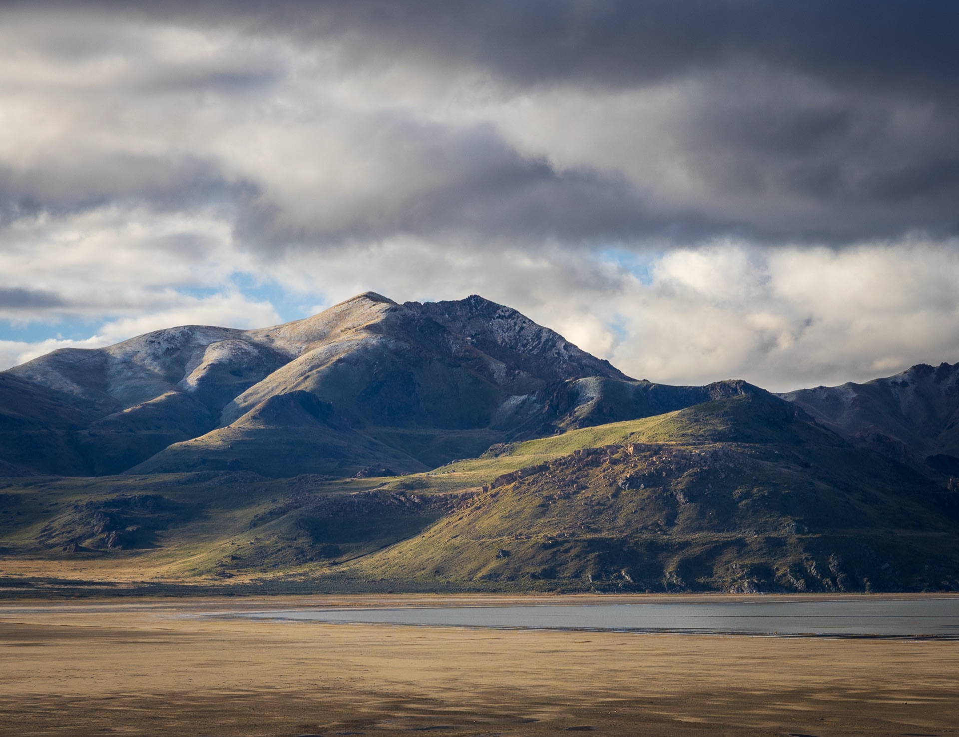 A snow-dusted mountain rising over a still lake and open plain